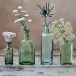 three green and one blue glass vases with flowers inside
