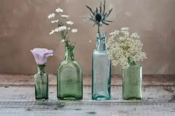 three green and one blue glass vases with flowers inside